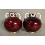 A pair of globular red glass vases with white formed handles and decorative rims in pink, blue and