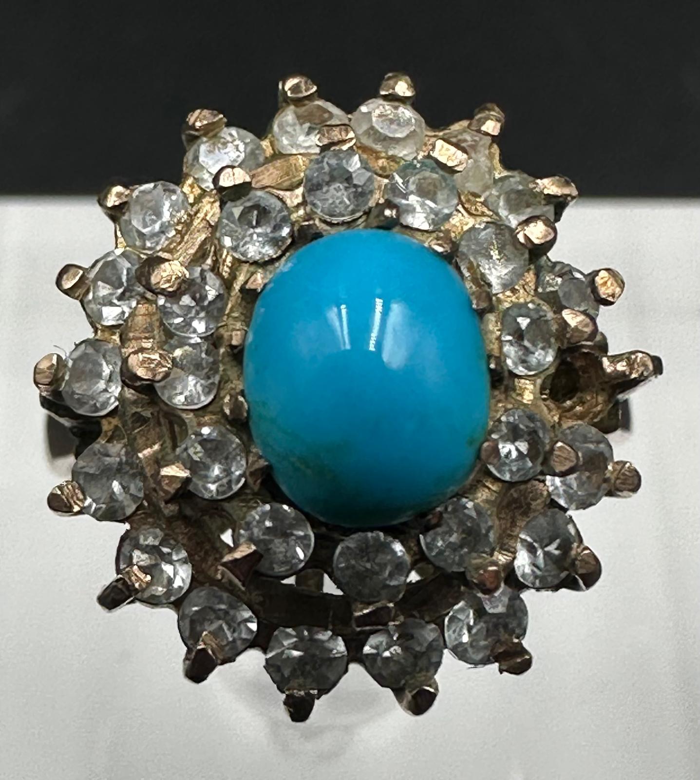 A turquoise central stone ring surrounded by clear stones on gold metal setting. - Image 2 of 3