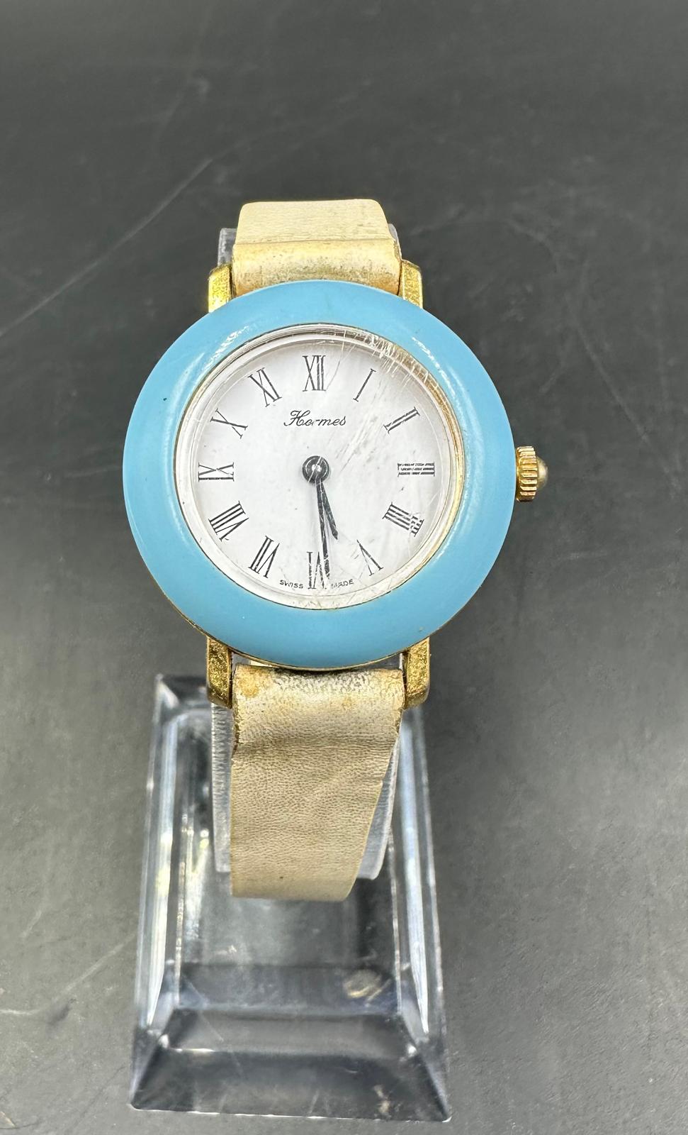 A vintage Hermes, blue bezel watch on stainless steel with white leather strap.