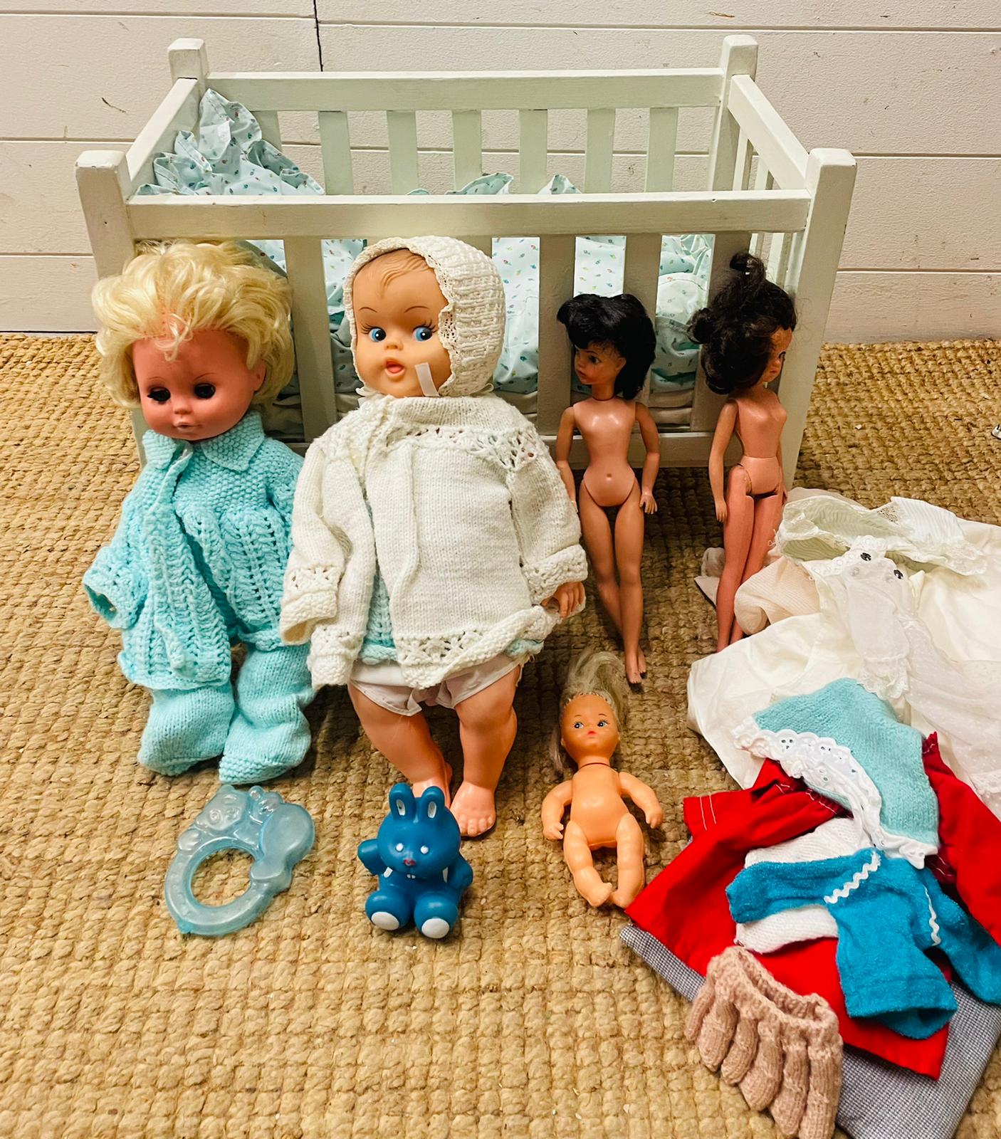 A vintage white wooden children's toy doll cot with dolls, bedding and toys