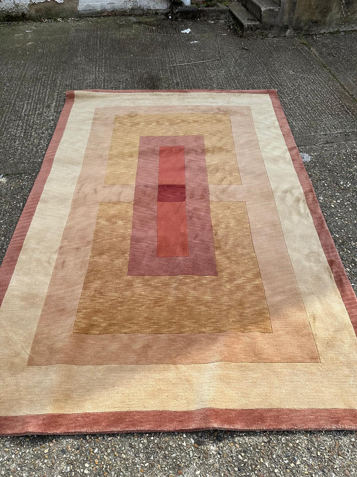 A beige ground wool rug in red, brown and orange 300cm x 210cm