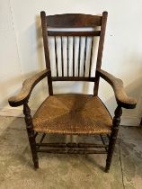 An oak rush seated spindle back open arm chair in the Arts and Crafts style
