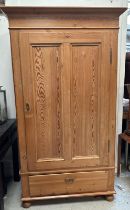 A pine single door wardrobe opening to a single cross hanging rail with drawer under (H178cm