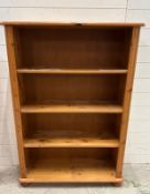 A pine three shelf bookcase on bun feet (H125cm W87cm D29cm)