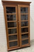 An Indian hardwood cabinet with glazed doors opening to six shelves and on bun feet (H209cm W120cm