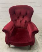 A burgundy upholstered button back arm chair on castors