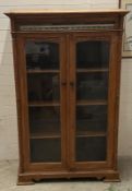 An Indian hardwood glazed cabinet with two doors opening to three long shelves, the cornice set with