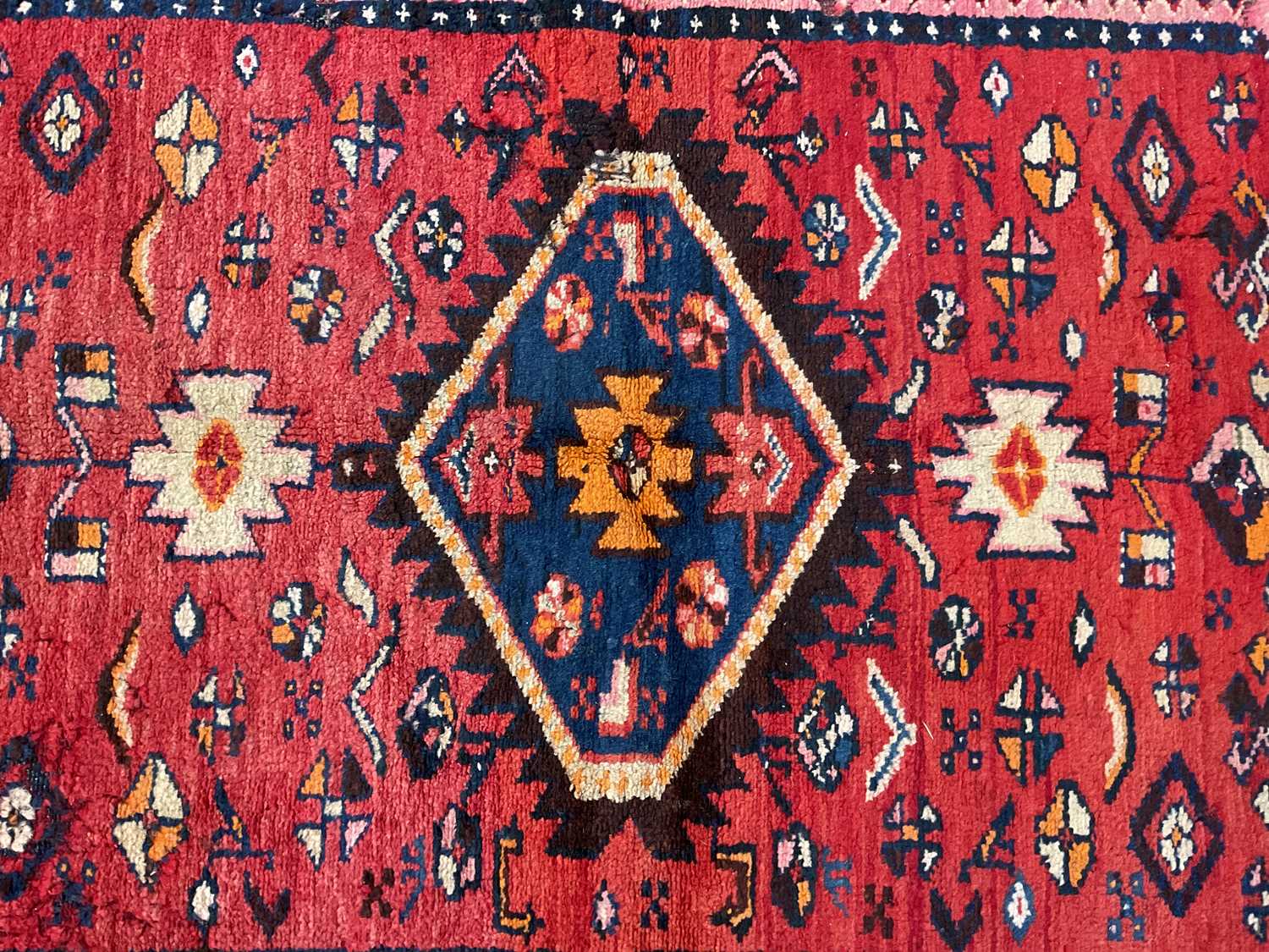 An antique Persian red ground carpet, with central triangular medallion surrounded by blue and red - Image 2 of 4