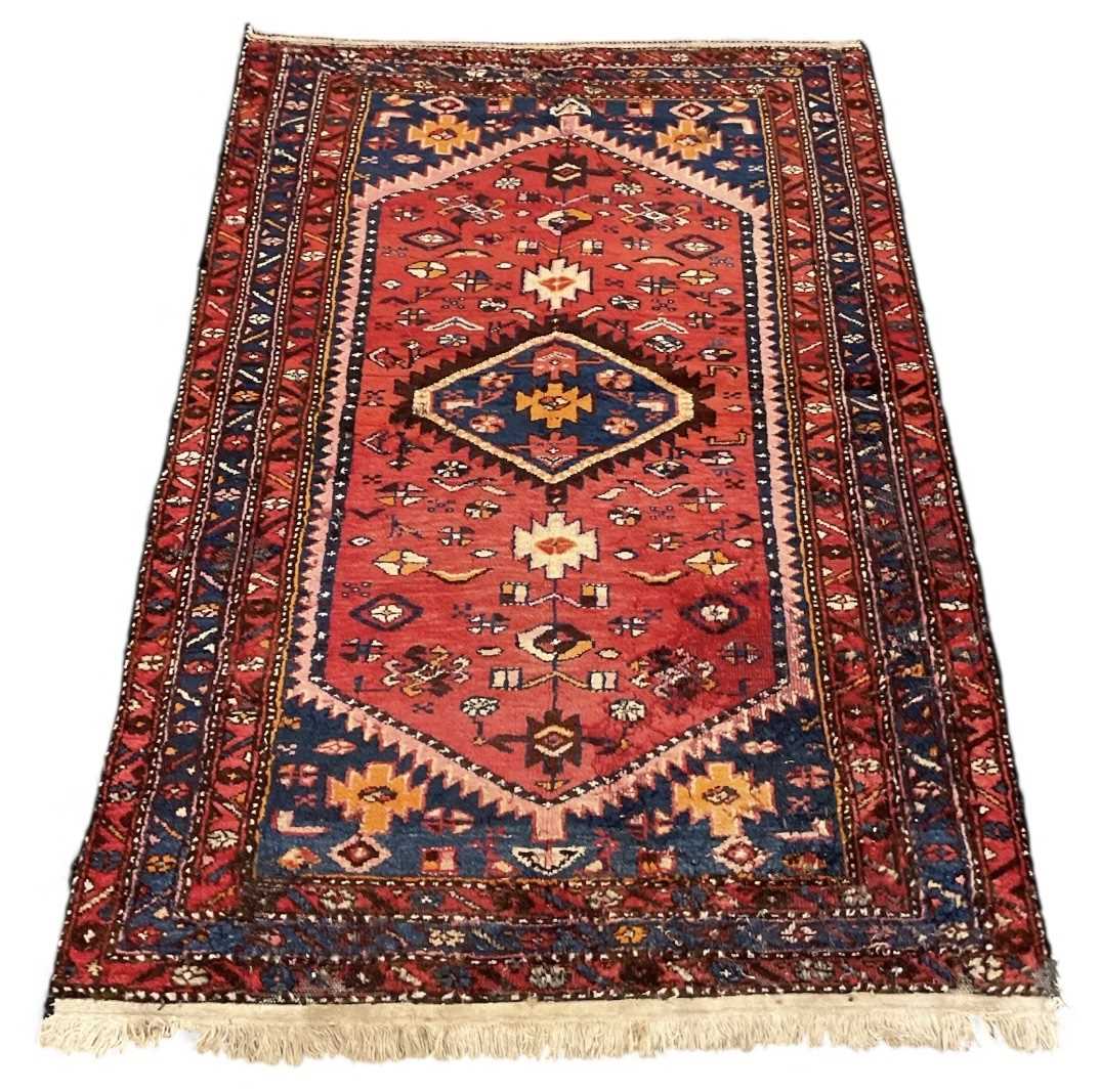 An antique Persian red ground carpet, with central triangular medallion surrounded by blue and red