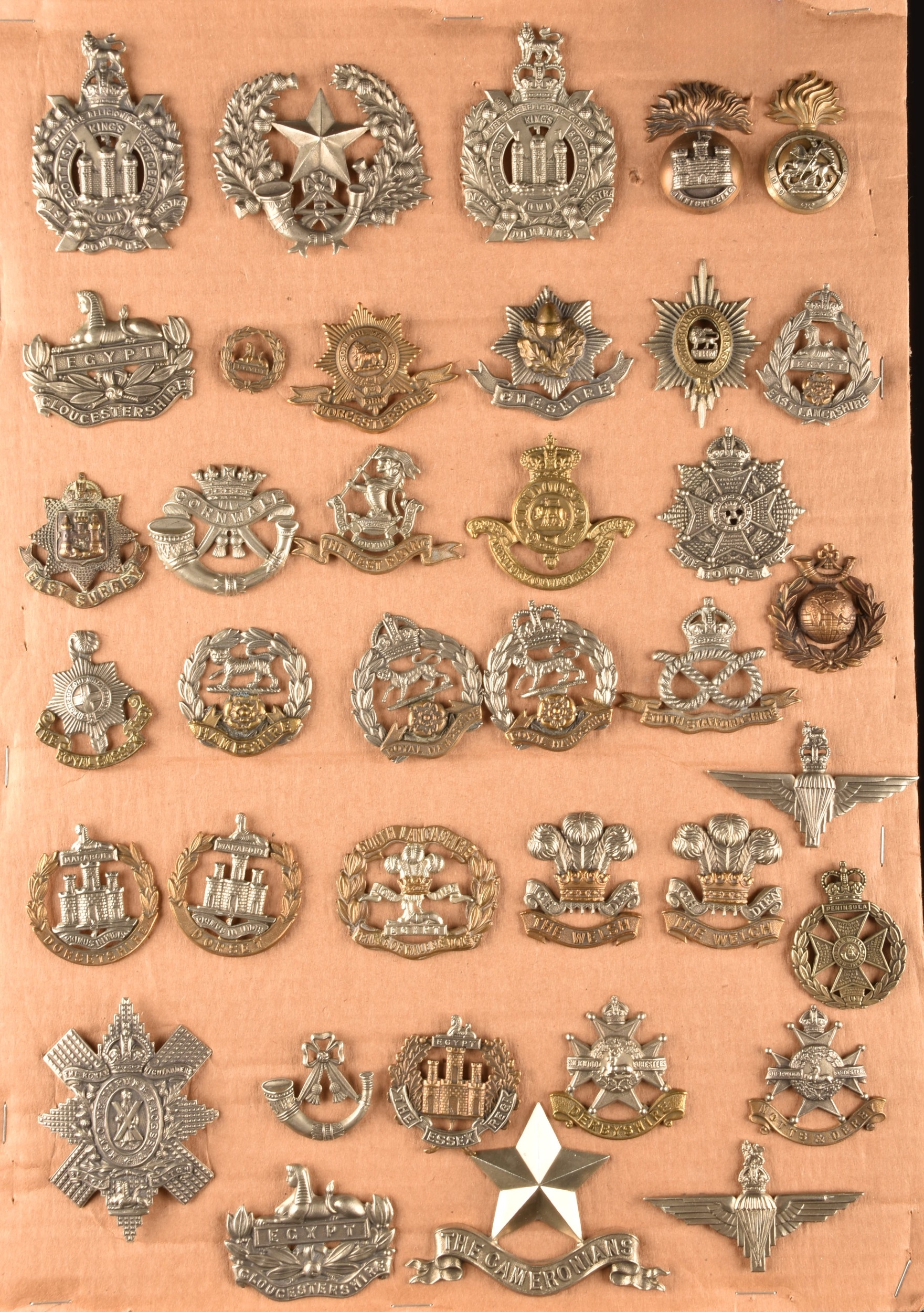 A collection of military cap badges, in cluding King's Own Scottish Borders, Gloucestershire