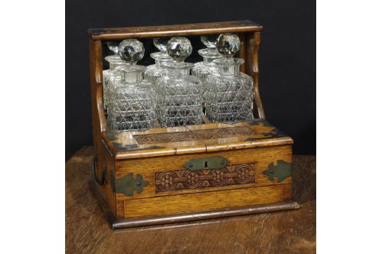 An Art & Crafts period oak tantalus cabinet, the three cut glass decanters restrained within a - Image 1 of 2