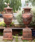 A pair of substantial faux terracotta garden urns on plinths,