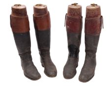 Two pairs of black leather riding boots. Both with red collars and in wooden trees.