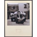A monochrome photograph of Mick Jagger and his Aston Martin, mounted with an autograph,