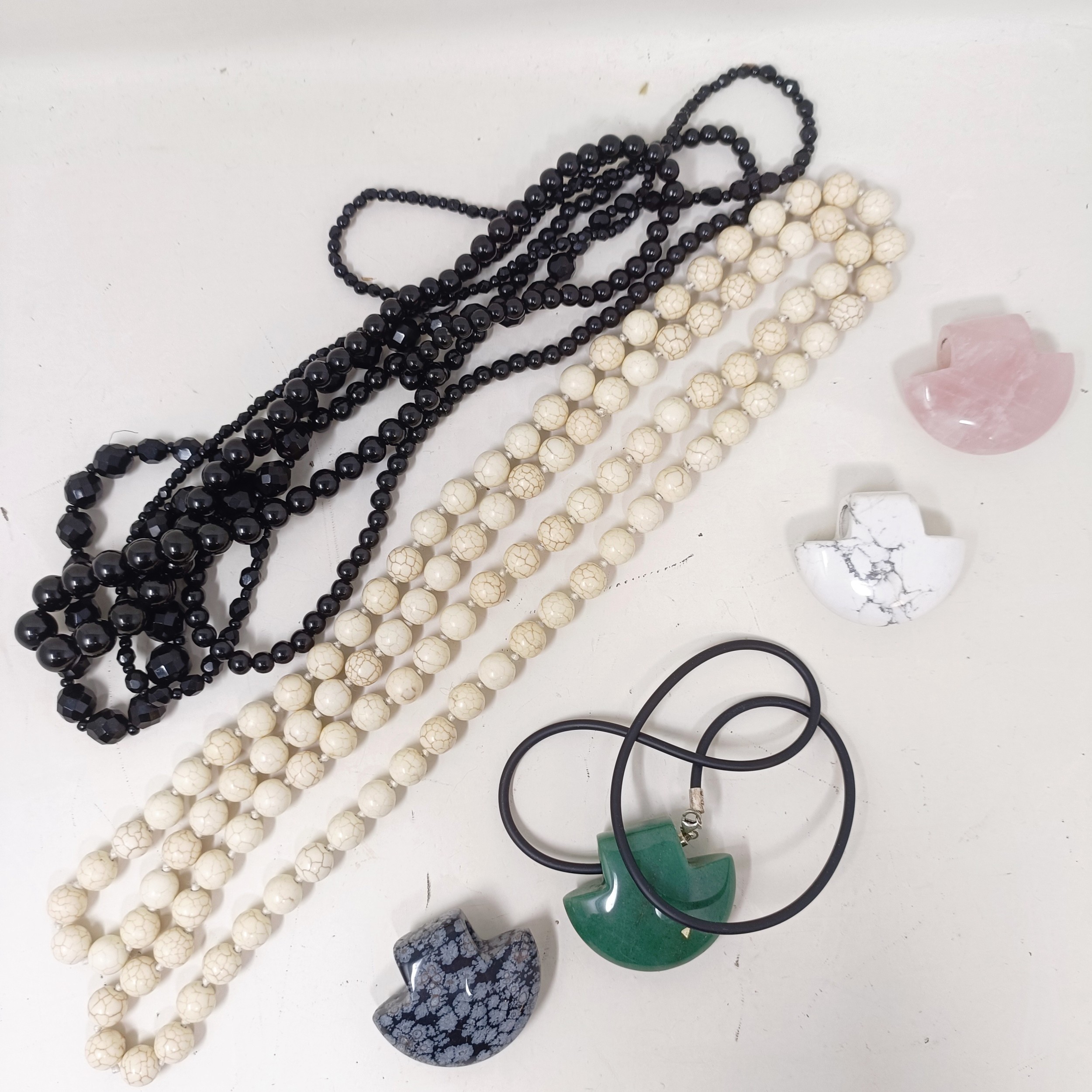 A pale stone bead necklace, a set of four matching carved stone pendants, and two black bead