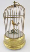 20th century gilt metal birdcage automaton with feathered bird on branch above foliage, the base
