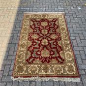 A 20th century rug with all-over scrolling foliate decoration over an iron red ground within a