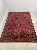 A Persian carpet with flowerhead design across the burgundy field within foliate spandrels and
