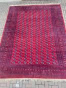 A large bokhara carpet with repeating gul motifs across a burgundy field within multiple stylised