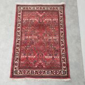A Persian rug with stylised foliate design on a burgundy field within flowerhead borders. L.155 W.
