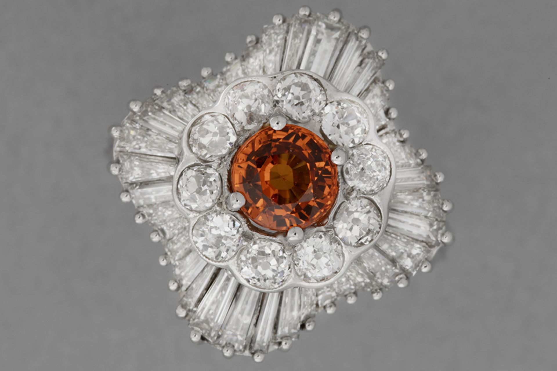 classy cocktail ring in platinum with a ca 1,30 carat orange sapphire surrounded by ca 3 carat of ve
