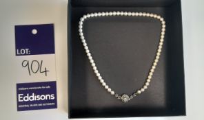 A pearl necklace featuring a rose of diamonds, inside a black box