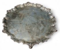 A large silver shaped circular salver, scroll feet, the field inscribed Presented to W H Gilbert Esq