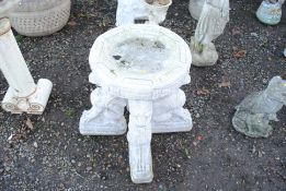 A cast concrete bird bath raised upon four seated