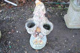 A painted concrete statue of a gnome holding two b
