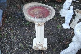 A tall concrete and painted bird bath raised on co