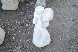 A concrete statue of a seated child holding a wate