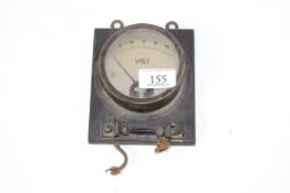 A brass volt meter set to a wooden plaque