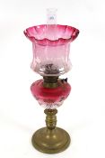 An ornate oil lamp, a brass based oil lamp with decorative ceramic reservoir and ornate cranberry
