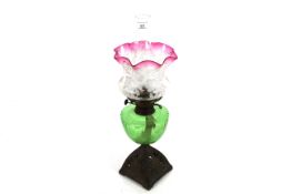An ornate Victorian oil lamp with brass base, green reservoir and ornate shade with cranberry