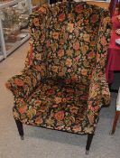 A late 19th / early 20th Century wing back armchair, upholstered in floral stamped velour, raised on