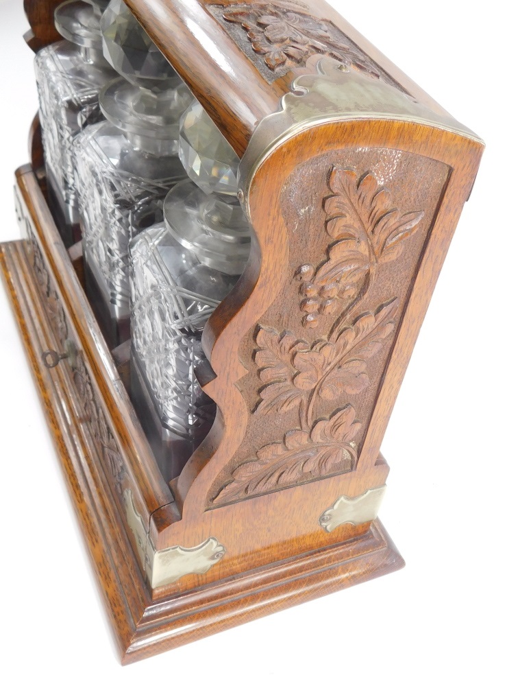 An Edwardian carved oak tantalus, with silver plated mounts, containing three square section cut - Image 3 of 3