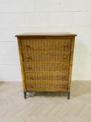 A tall contemporary wicker work chest of drawers with a hardwood top
