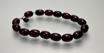 A stand of fourteen dark cherry amber beads, each approximately: l. x 3cm and a smaller bead: l. x