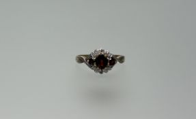 A 9ct gold ring set oval red cut stone flanked by a red stone to each shoulder in white metal