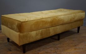 A contemporary upholstered bench stool, covered in mustard yellow velvet fabric with buttoned top