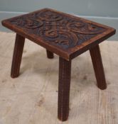 A 1920s carved oak stool, with relief carved top featuring scrolling vine and leaf decoration,