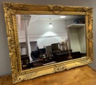 A reproduction gilt mirror in the Rococo style, with ornate moulded scrolls and foliage and bevelled