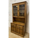 A modern two-part kitchen dresser by Ercol, with carved cornice over twin glazed panel doors to top,