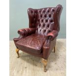 A 20th century leather wingback armchair, curved top over button back, rolled arms with brass stud