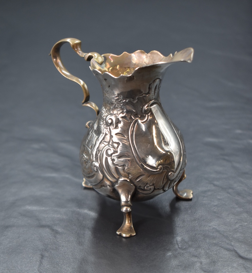 A Georgian silver cream jug, of bulbous form having a Chippendale style rim, shallow spout opposed