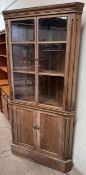 An oak corner cupboard with a moulded cornice and glazed doors,