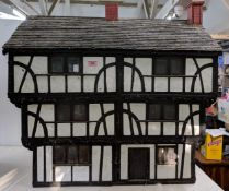A handmade Tudor style dolls house with half timbered decoration, a pitched roof with two