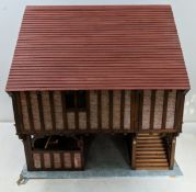 A handmade, two storey Tudor style dolls house with a pitched roof covered in red tiles, an