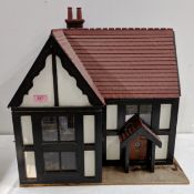 A handmade Tudor style dolls house, featuring half timbering with black beams and white panels, a