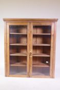 A C19th stripped pine hanging cabinet with two glazed doors, 101 x 33 x 124cm